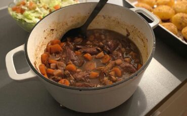 En stor vit gryta med vegansk Boeuf Bourguignon som serveras med potatis och sallad