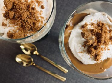 Vegansk Biscoff cheesecake i glas, elegant serverad med lager av krämig fyllning och krossade Biscoff-kex, toppad med ett helt kex och några smulor för dekoration